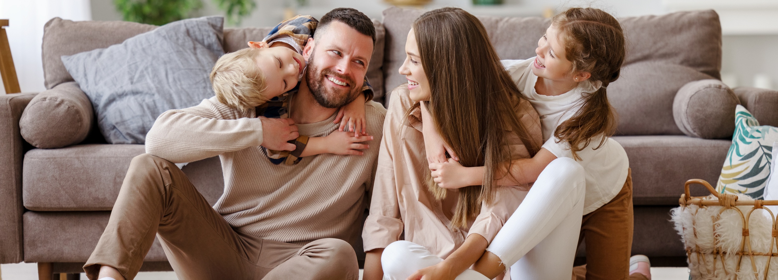 Eine glückliche Familie mit Vater, Mutter und zwei Kindern sitzt zu Hause auf dem Fußboden vor einem Sofa.