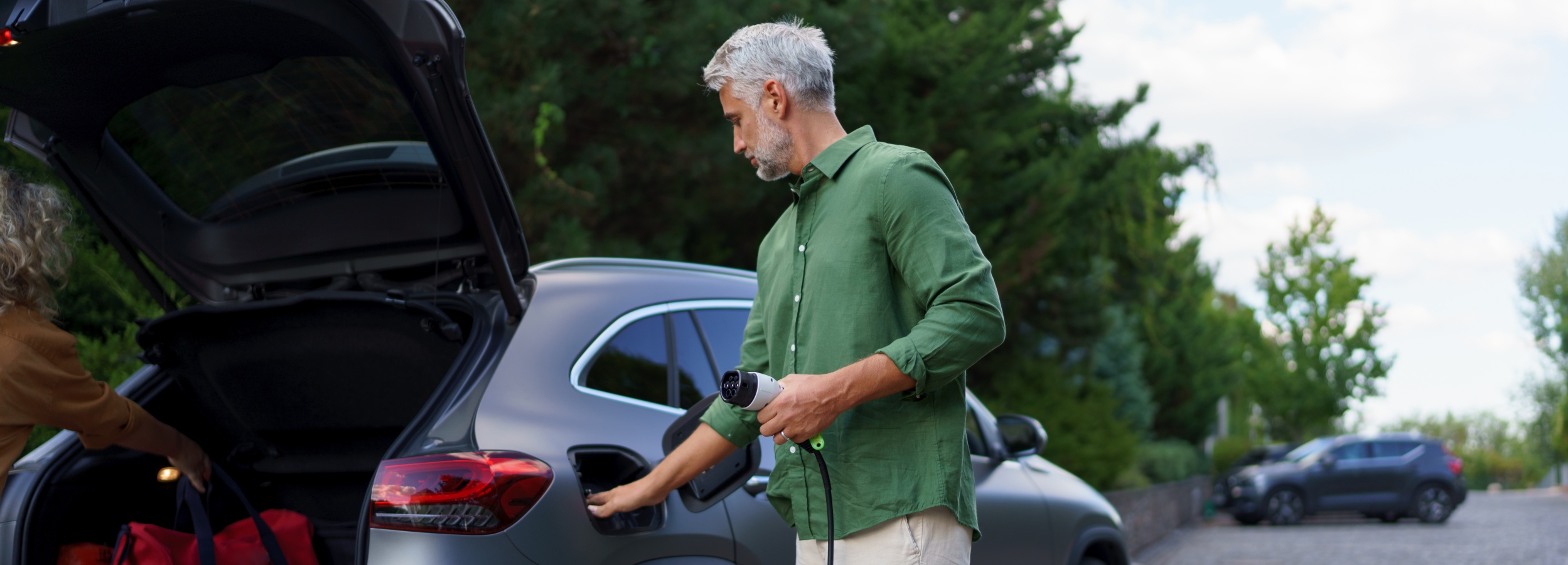 Ein Mann hält ein Ladekabel in der Hand, mit dem er ein Elektrofahrzeug aufladen will.